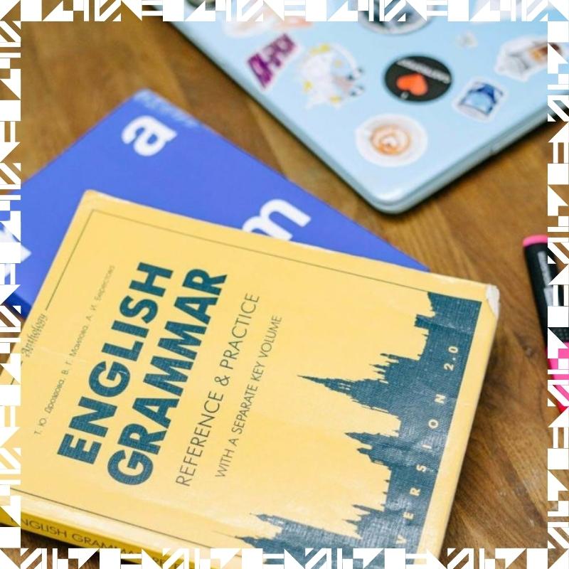 An English grammar book on top of a desk next to a laptop.