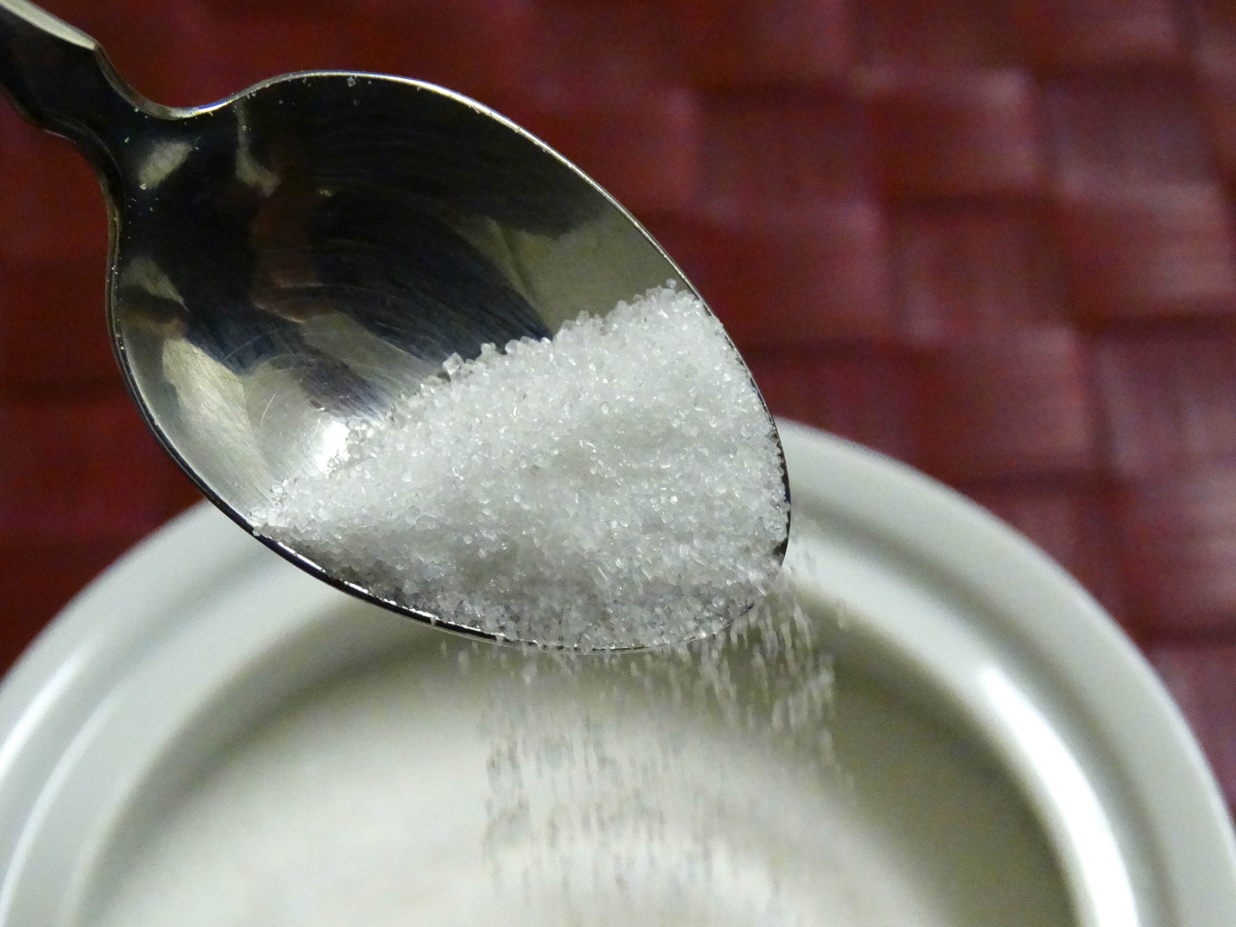 A spoonful of white sugar is being emptied back into a white container.