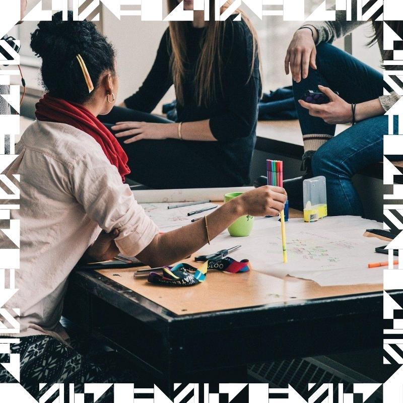 Three students with a bunch of papers, pencils, and crayons spread across a working table